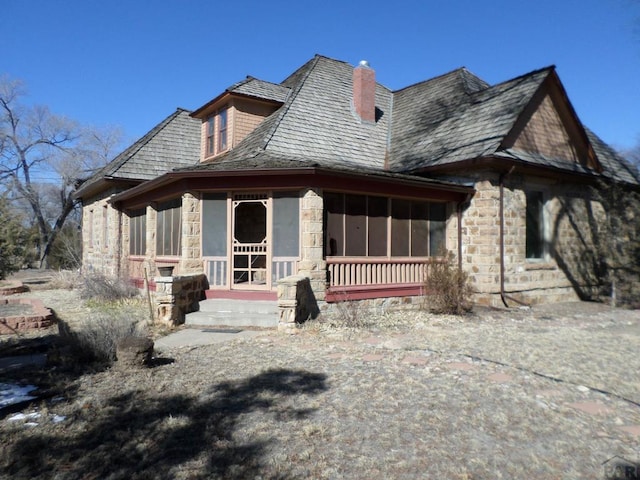 view of front of house with a sunroom, stone siding, and a chimney