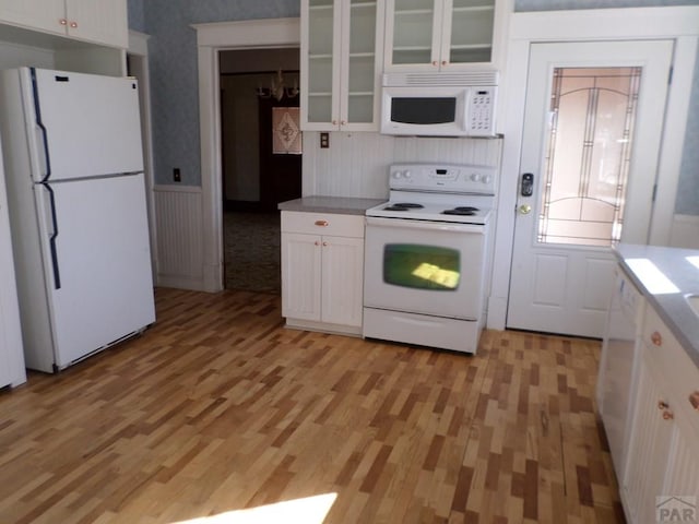 kitchen with white appliances, wallpapered walls, light wood finished floors, white cabinets, and glass insert cabinets