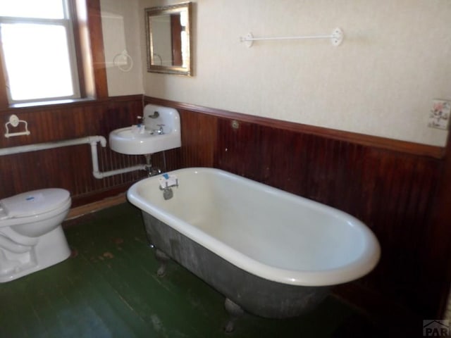 bathroom featuring wooden walls, wainscoting, toilet, wood finished floors, and a freestanding bath