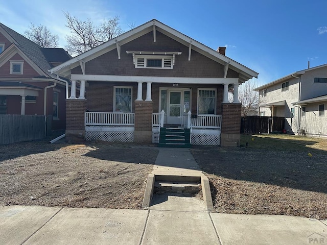 view of front of property featuring covered porch, a chimney, fence, and brick siding