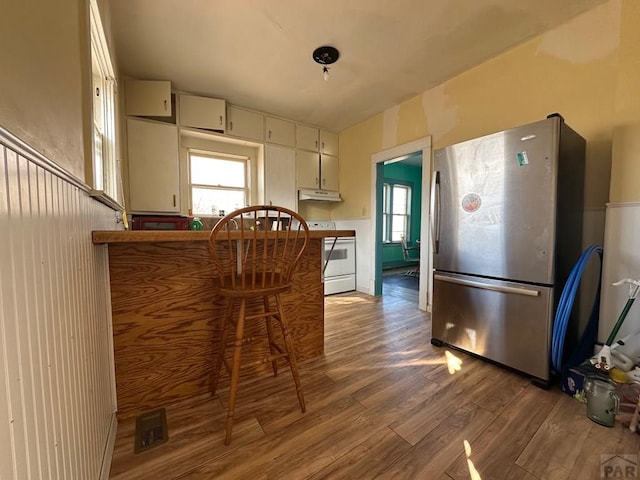 kitchen featuring white electric range, freestanding refrigerator, white cabinetry, wood finished floors, and under cabinet range hood