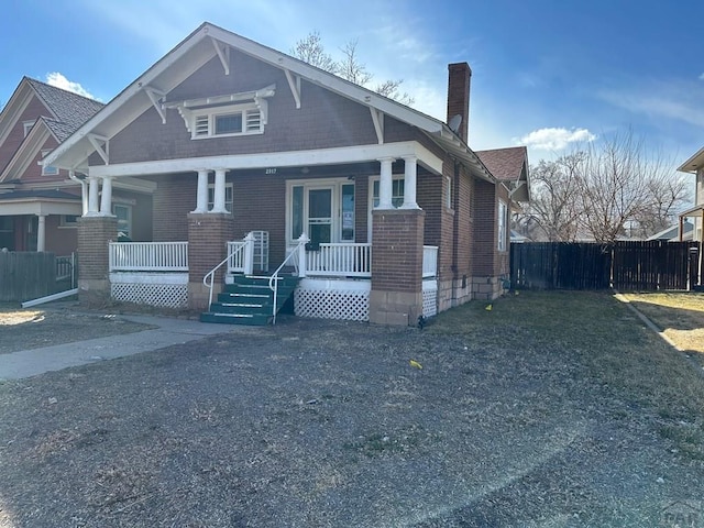 view of front of house featuring a chimney, fence, a porch, and brick siding