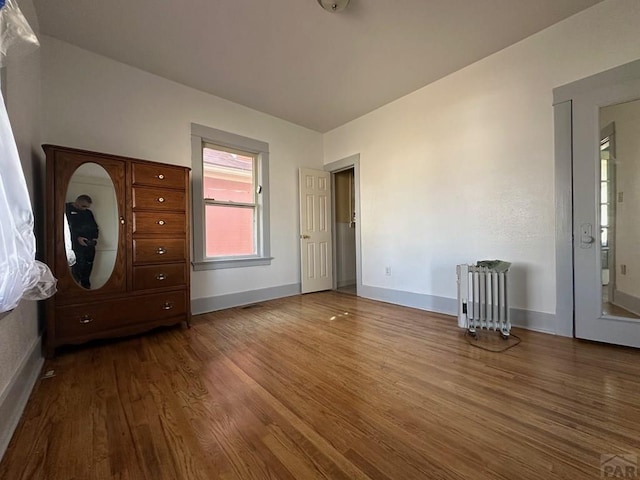 unfurnished bedroom with dark wood-type flooring, radiator heating unit, and baseboards