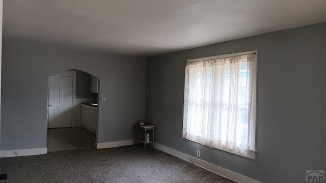 carpeted empty room featuring arched walkways and baseboards