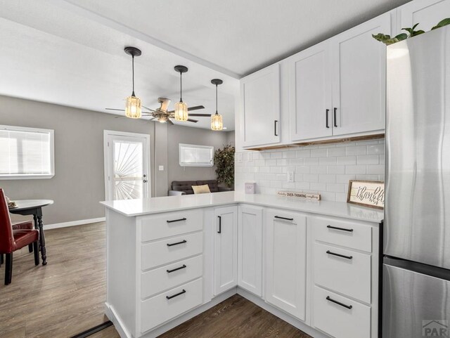 kitchen with tasteful backsplash, light countertops, a peninsula, freestanding refrigerator, and dark wood-style flooring