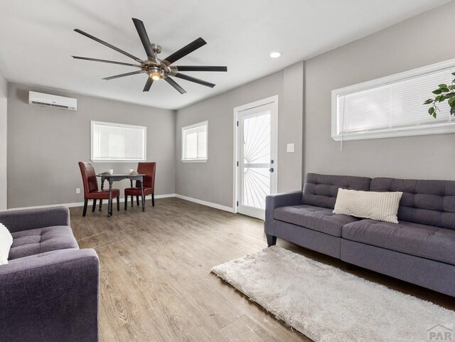 living room with a ceiling fan, a wall mounted air conditioner, baseboards, and wood finished floors