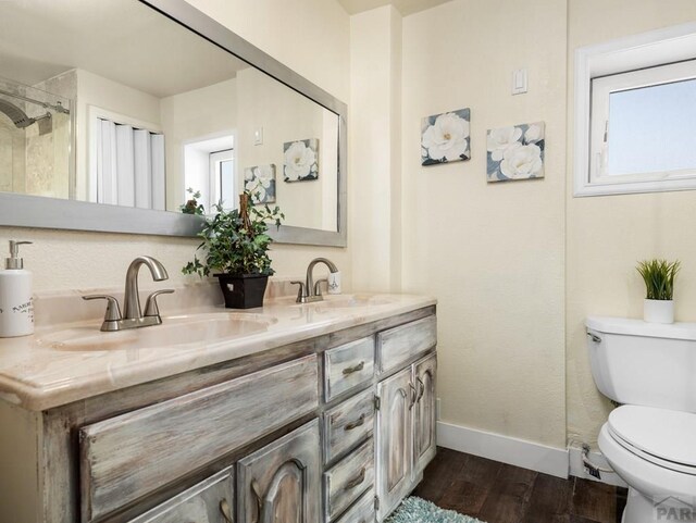 full bath featuring double vanity, a sink, baseboards, and wood finished floors