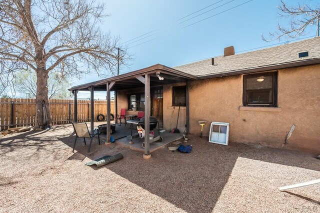 back of house featuring roof with shingles, stucco siding, a patio area, fence, and a fire pit