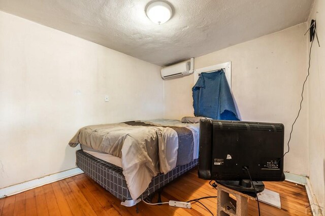 bedroom featuring a wall unit AC, a textured ceiling, baseboards, and wood finished floors