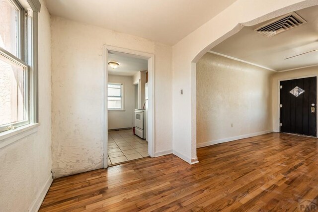 foyer featuring arched walkways, light wood-type flooring, visible vents, and baseboards