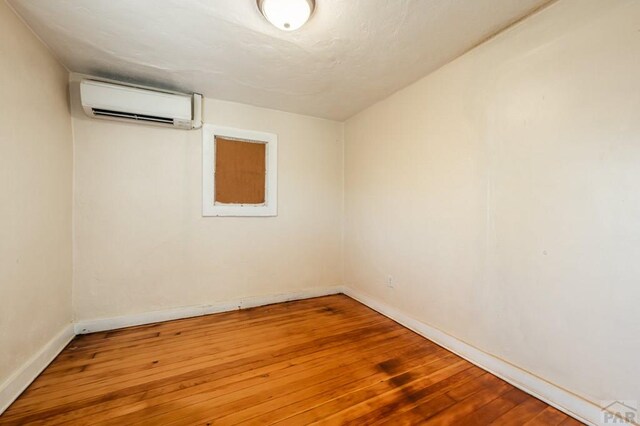 empty room with a wall mounted AC, wood finished floors, and baseboards