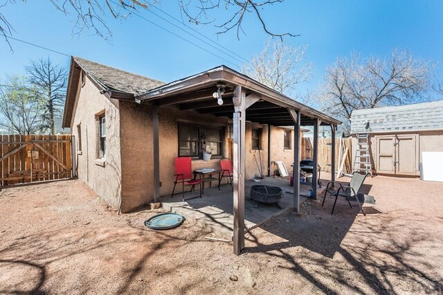 rear view of house featuring an outdoor fire pit, fence, a shingled roof, and stucco siding