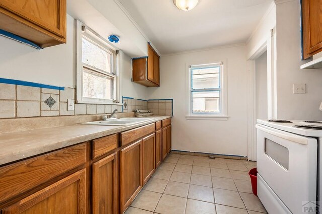 kitchen with plenty of natural light, white range with electric stovetop, brown cabinetry, light countertops, and a sink