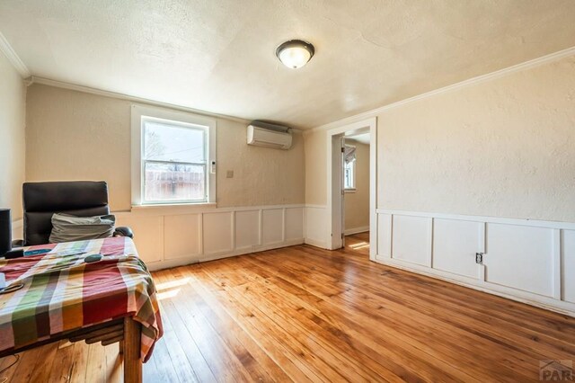 office featuring a textured wall, ornamental molding, a wall mounted air conditioner, a textured ceiling, and light wood-style floors