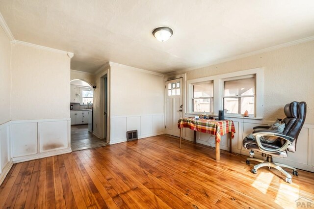 office with arched walkways, ornamental molding, a wainscoted wall, and light wood-style flooring