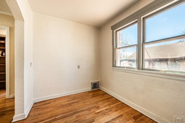 empty room featuring baseboards, visible vents, wood finished floors, and a textured wall