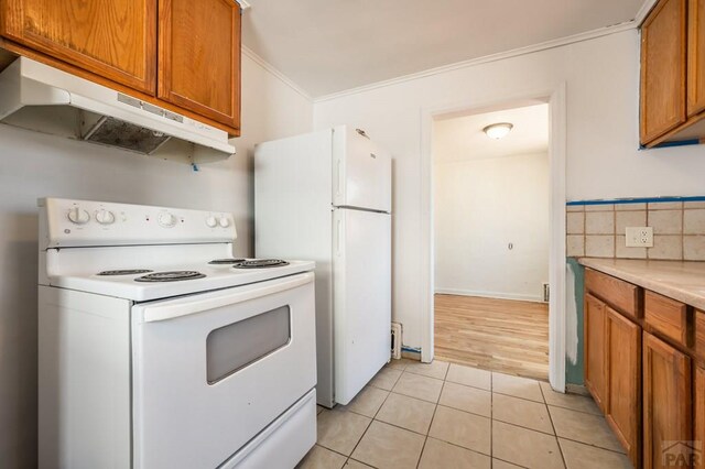 kitchen with white appliances, light tile patterned floors, ornamental molding, light countertops, and under cabinet range hood