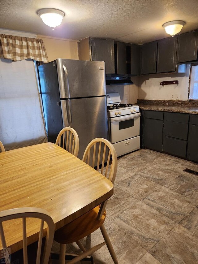 kitchen featuring gas range gas stove, dark countertops, visible vents, freestanding refrigerator, and under cabinet range hood