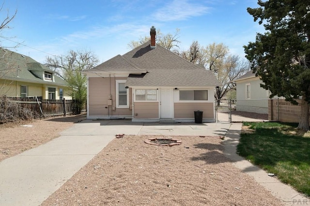 rear view of property featuring a chimney, fence, a gate, and a shingled roof