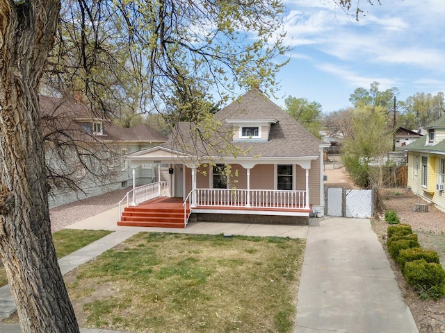 victorian home with a front lawn, covered porch, roof with shingles, concrete driveway, and fence