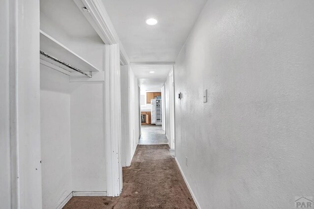 hallway featuring baseboards, wood finished floors, and a textured wall