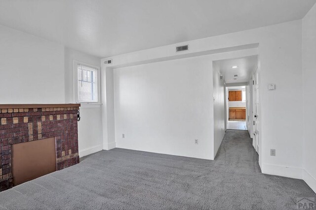 unfurnished living room featuring dark colored carpet, a brick fireplace, and visible vents