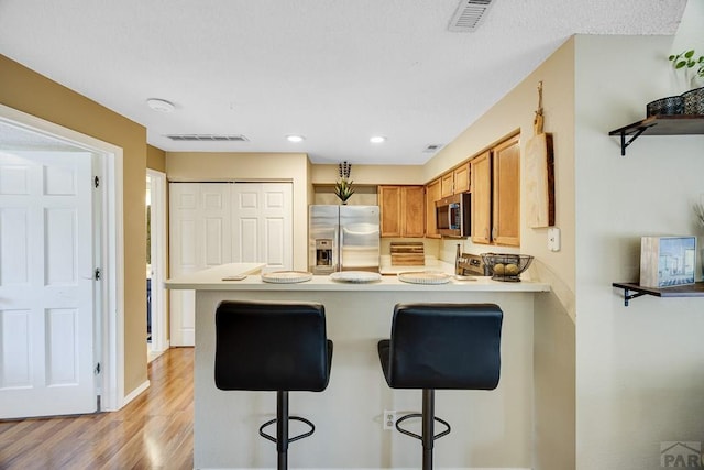 830 S Vance St, Lakewood, CO 80226 - kitchen featuring appliances with stainless steel finishes, a peninsula, light wood-style flooring, a breakfast bar area, and brown cabinetry