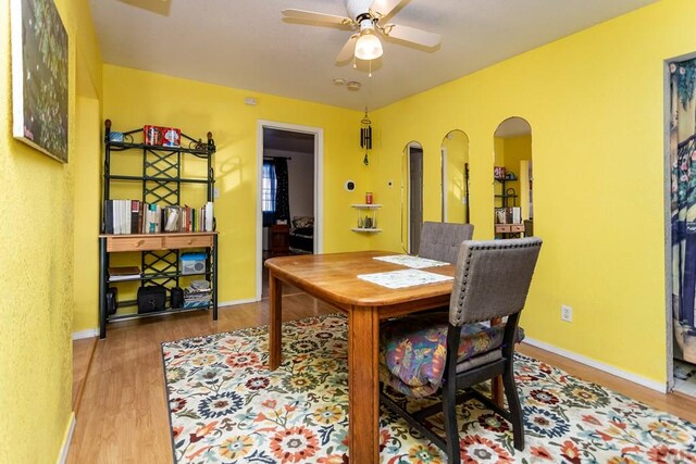 dining room featuring baseboards, ceiling fan, arched walkways, and wood finished floors