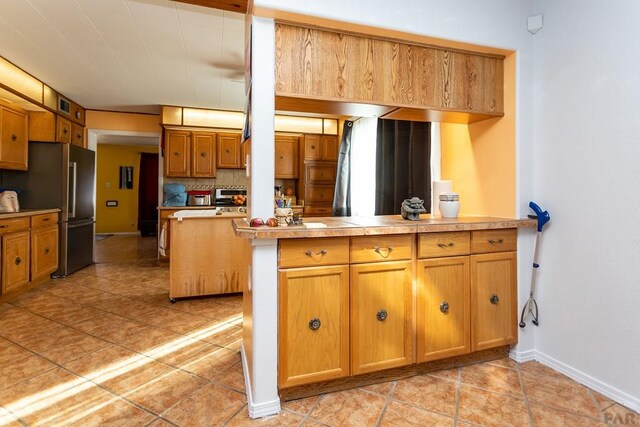 kitchen with brown cabinetry, freestanding refrigerator, light countertops, and a peninsula