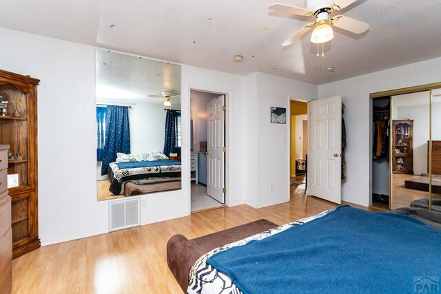 bedroom featuring ceiling fan, ensuite bathroom, wood finished floors, visible vents, and a closet