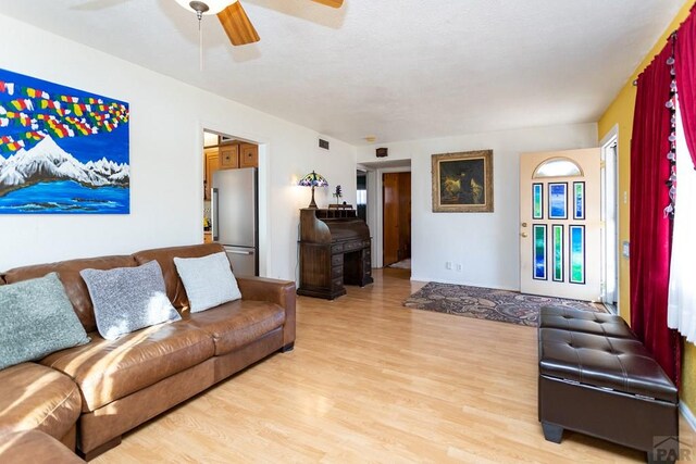 living room with light wood-type flooring, visible vents, and ceiling fan