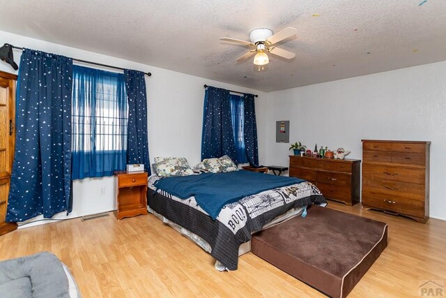 bedroom with light wood-type flooring, electric panel, a ceiling fan, and a textured ceiling