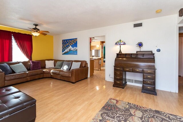 living area featuring light wood-type flooring, baseboards, visible vents, and a ceiling fan