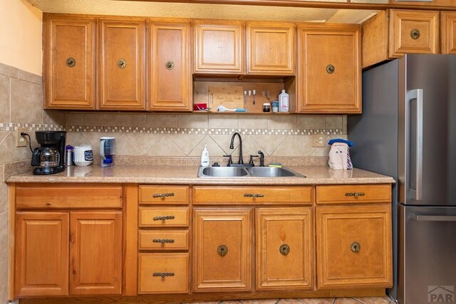 kitchen featuring brown cabinetry, light countertops, a sink, and freestanding refrigerator