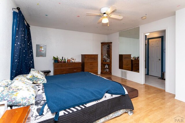 bedroom featuring light wood-type flooring, ceiling fan, electric panel, and visible vents