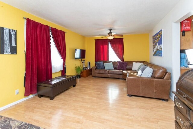 living area with baseboards, ceiling fan, and light wood finished floors