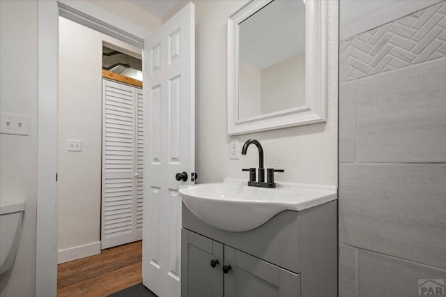 bathroom featuring baseboards, wood finished floors, toilet, and vanity