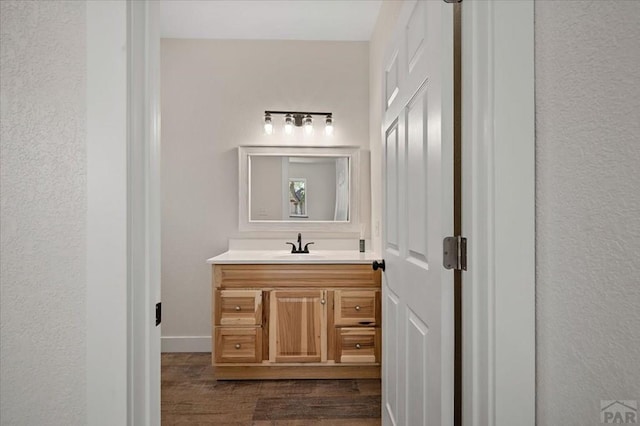 bathroom with a textured wall, vanity, and wood finished floors