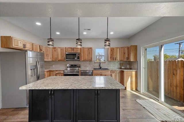 kitchen featuring stainless steel appliances, light countertops, backsplash, wood finished floors, and a kitchen island