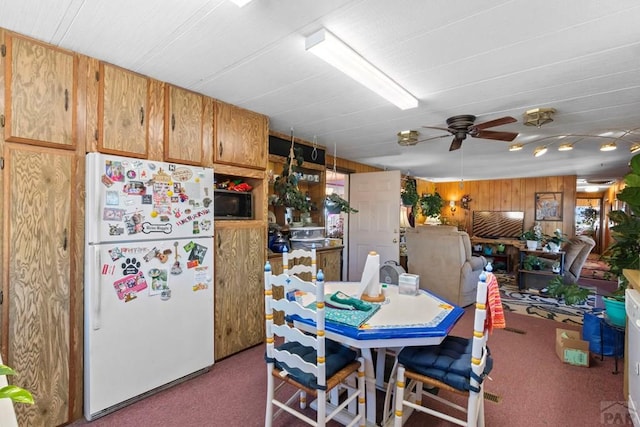 dining area with a ceiling fan, carpet flooring, and wooden walls