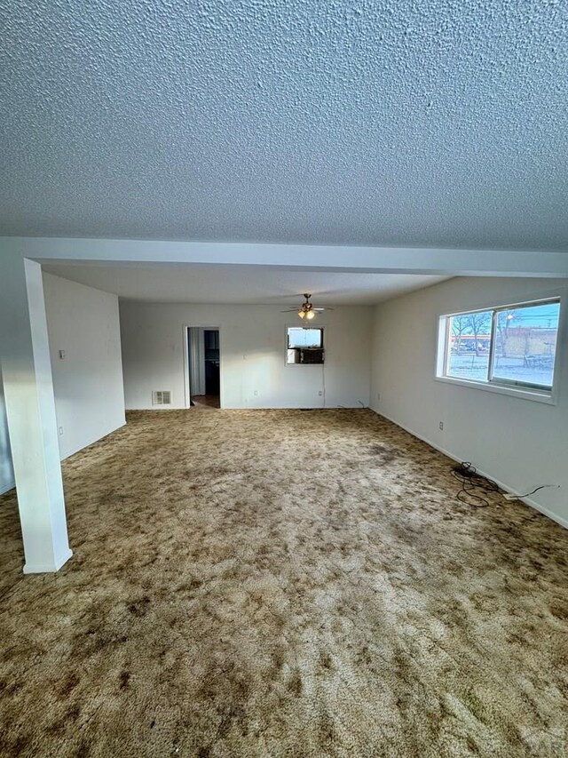 unfurnished room with carpet, visible vents, ceiling fan, and a textured ceiling