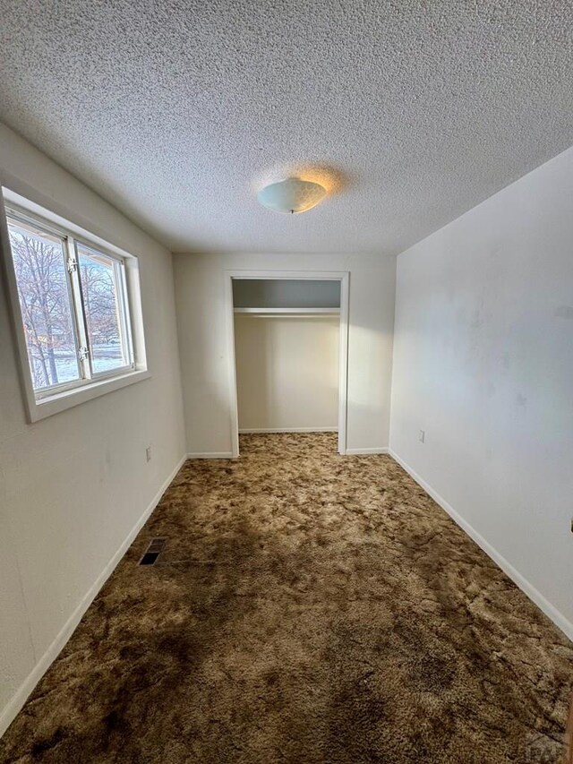 unfurnished bedroom with baseboards, visible vents, a textured ceiling, carpet floors, and a closet