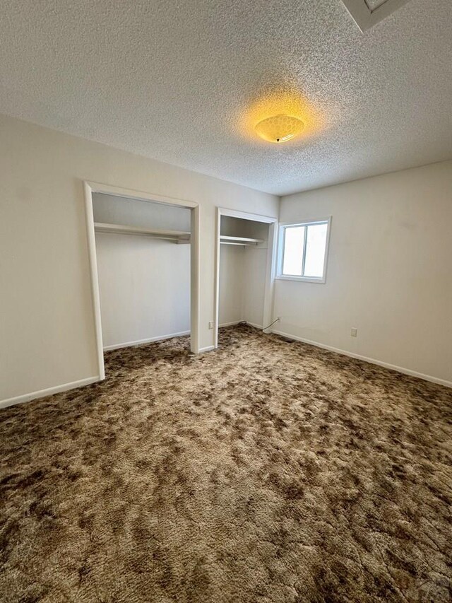 unfurnished bedroom with a textured ceiling, baseboards, multiple closets, and carpet flooring