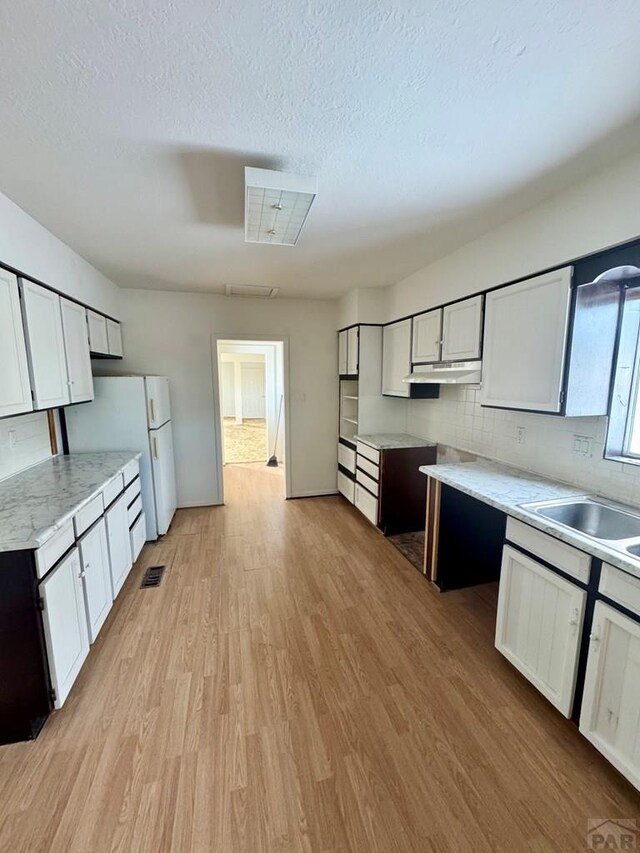 kitchen with light wood finished floors, light countertops, under cabinet range hood, white cabinetry, and backsplash