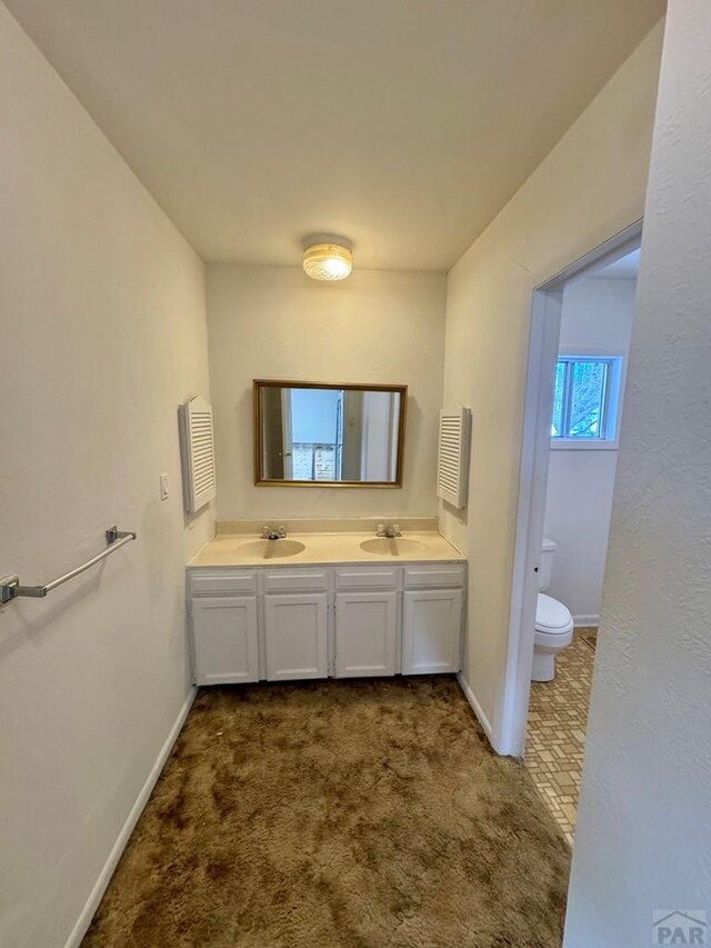 bathroom featuring a sink, double vanity, toilet, and carpet flooring