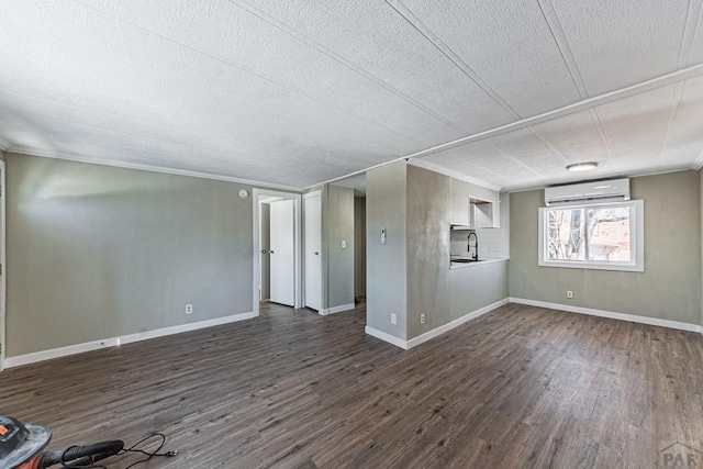 unfurnished living room with a wall mounted air conditioner, baseboards, dark wood-type flooring, and a sink