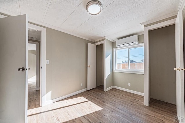 unfurnished bedroom featuring ornamental molding, a wall mounted AC, a textured ceiling, wood finished floors, and baseboards