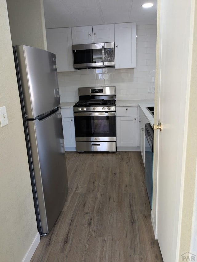 kitchen featuring wood finished floors, decorative backsplash, light countertops, white cabinets, and appliances with stainless steel finishes