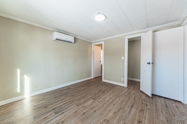 empty room with baseboards, an AC wall unit, wood finished floors, and crown molding