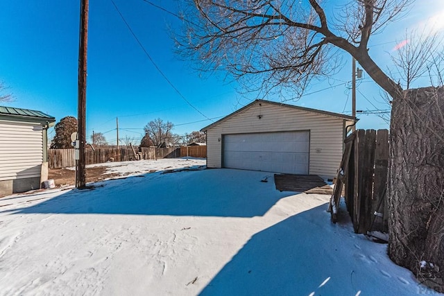 snow covered garage featuring a garage and fence